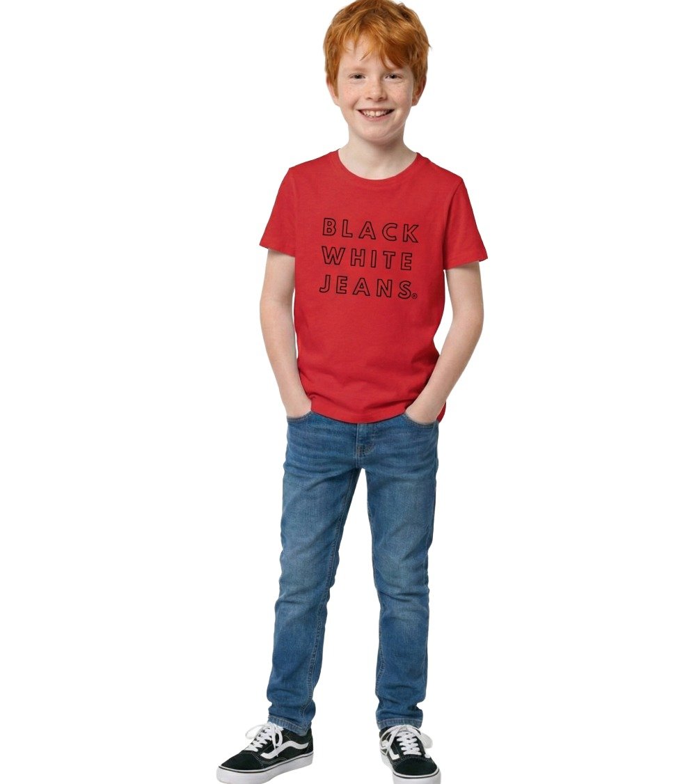 A smiling boy posing in the Black White Jeans Everyday kids organic red t-shirt featuring the signature black text logo, styled with blue jeans and skate shoes on a clean white background.