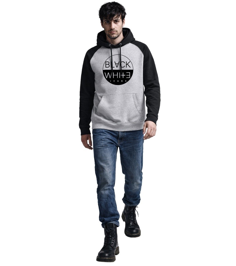 British male model wearing the Men's Varsity Raglan Hoodie in Grey and Black by Black White Jeans. Contrast raglan sleeve hoodie for men featuring chest logo, styled with blue denim jeans and black combat boots in a cinematic studio setting.